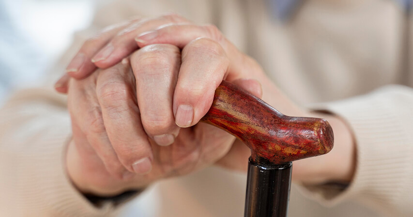 As mãos de um idoso segurando uma bengala