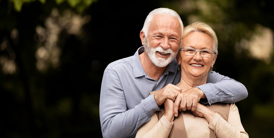 Um casal de idosos posando abraçados para a foto sorrindo