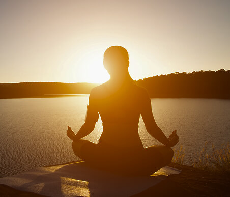 Imagem por trás de uma mulher meditando em frente ao por do sol