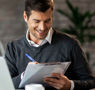 Homem sorridente escrevendo um relatório empresarial enquanto usa um Laptop