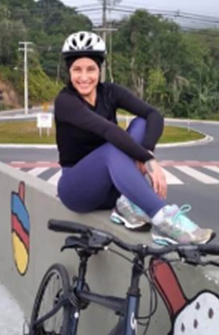 Vilma de Lurdes Carneiro sentada em uma mureta com sua bicicleta
