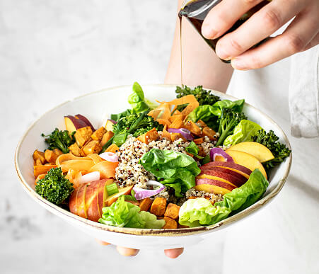 Mulher adicionando azeite a uma salada em um prato